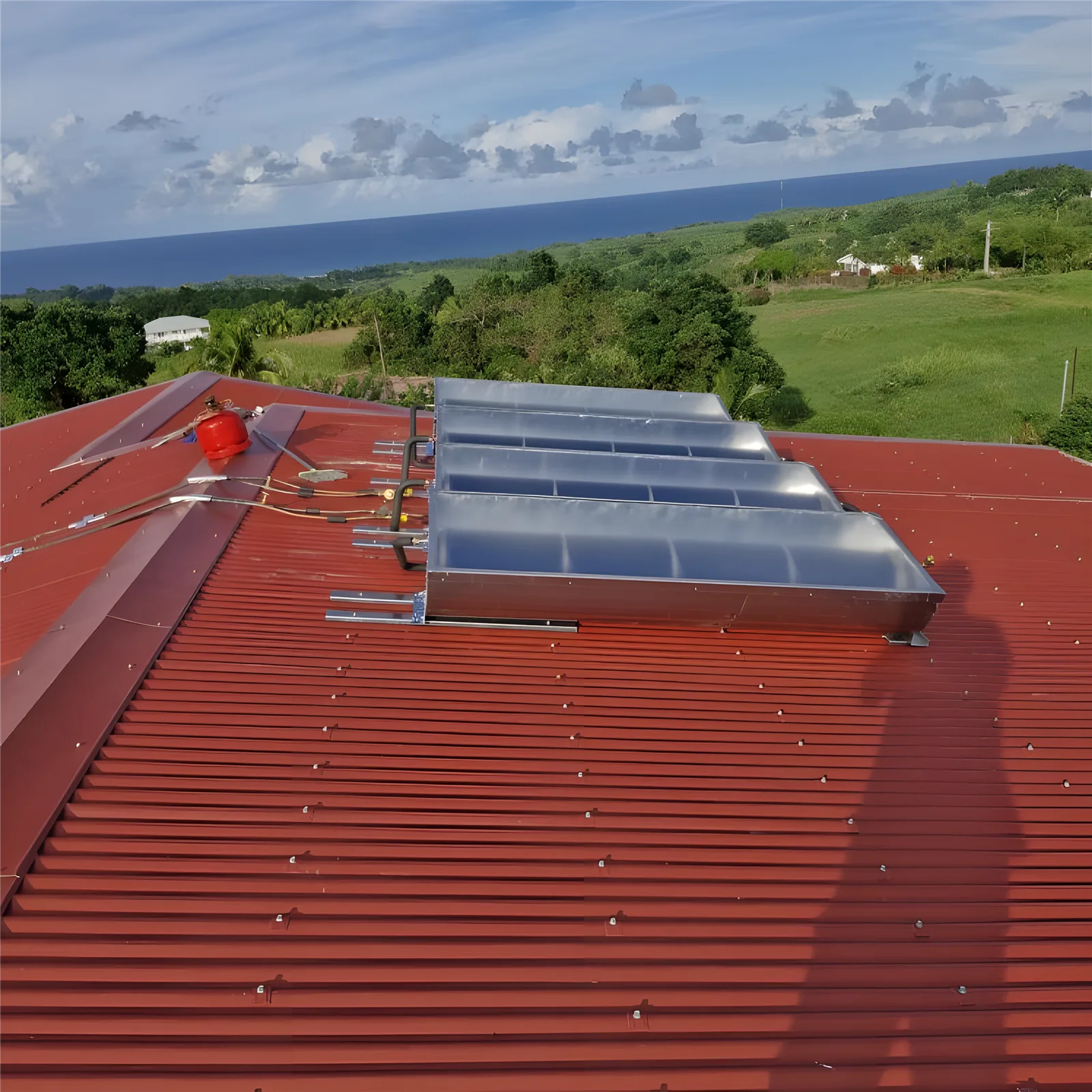 Capteurs solaires posés sur une toiture en tôle rouge, vue sur la mer